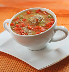 Home-made meatballs and vegetable soup, in a white soup cup