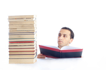 Young man with a pile of books reading one of them