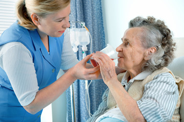 Nurse cares for a elderly woman lying in bed - obrazy, fototapety, plakaty