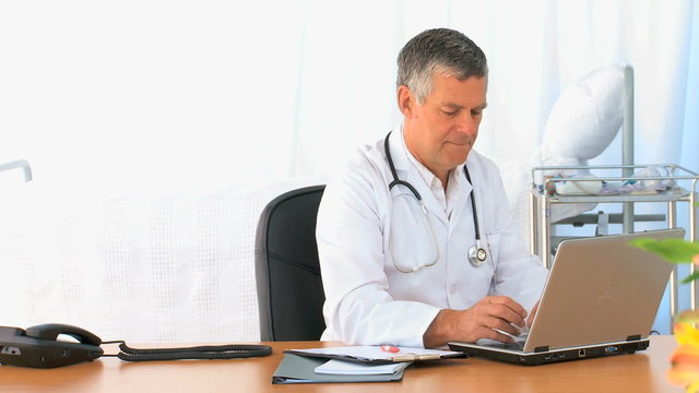 Mature doctor working on his laptop
