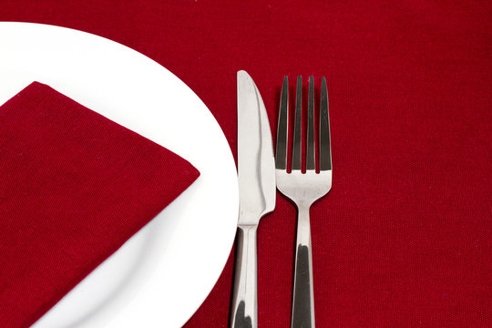 Knife and fork with white plate on red tablecloth