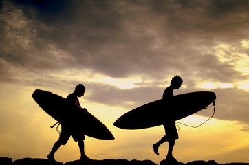 Two Surfers Carrying Their Boards Home At Sunset