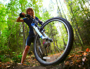 Young woman trying to ride on a bicycle in forest's offroad