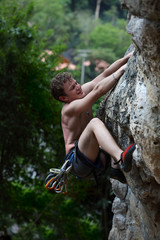 Young male climbing on a cliff on green trees background 