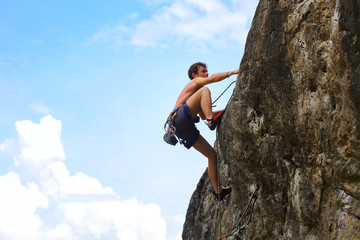 Young male climbing on a cliff on blue cloudy sky background