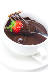 melted chocolate in a cup, fork and strawberries isolated on whi