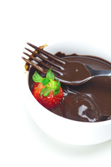 melted chocolate in a cup, fork and strawberries isolated on whi