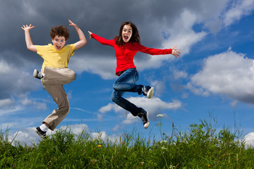 Fototapeta na wymiar Girl and boy jumping, running against blue sky