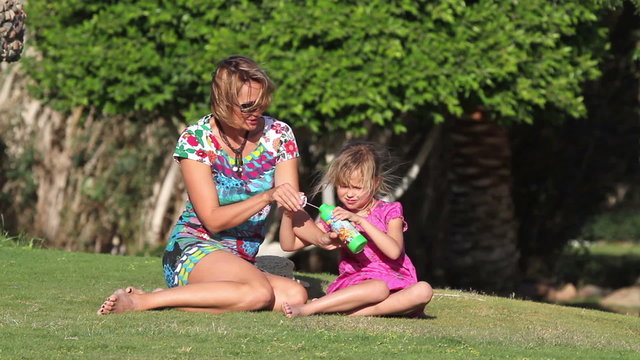 girl with her ​​mother on the lawn blow bubbles