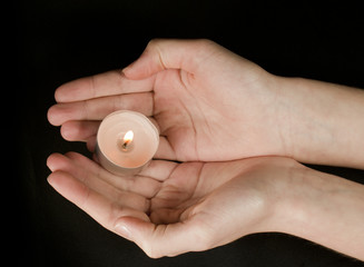 Hands holding a candle on black background