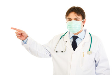 Medical doctor in mask pointing  up in corner at copy space
