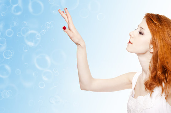 Red-haired girl tuching bubbles in the air.