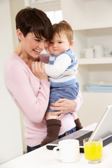 Woman With Baby Working From Home Using Laptop