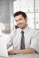 Happy office worker sitting at desk using laptop