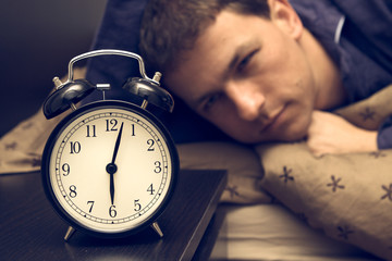 Alarm clock with male model in bed in background.