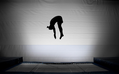 silhouette of jumping man on trampoline doing somersault