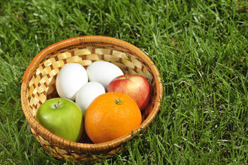 Wicker basket with fruits and eggs on grass