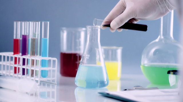 Scientist mixing chemicals in Erlenmeyer flask writing results