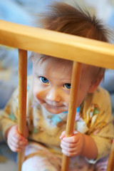 Small child sits in his wooden bed