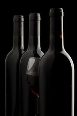 Elegant red wine glass and a wine bottles in black background