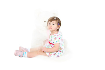 little girl sits on a white sheep skin with the big toy bear