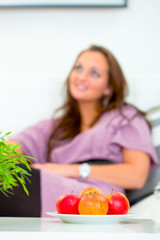 Fruit platter on table and woman sitting on sofa in background.