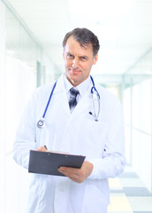 Happy smiling mature doctor writing on clipboard in a