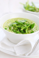Cream soup with asparagus, peas and leeks in white plate