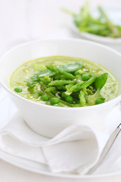 Cream soup with asparagus, peas and leeks in white plate