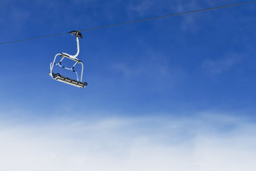 Single ski lift chair on bright blue sky with clouds