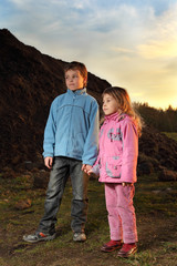 girl in pink clothes and boy in blue jacket standing near hill