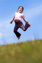 Girl jumping on the meadow, with blue sky and clouds in backgrou