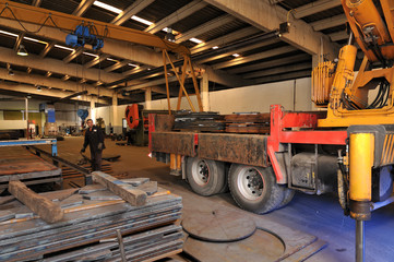 Crane loading truck at metal factory.