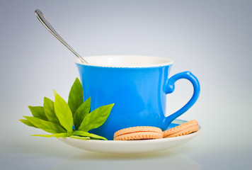 Blue tea cup with green leaves and cookies