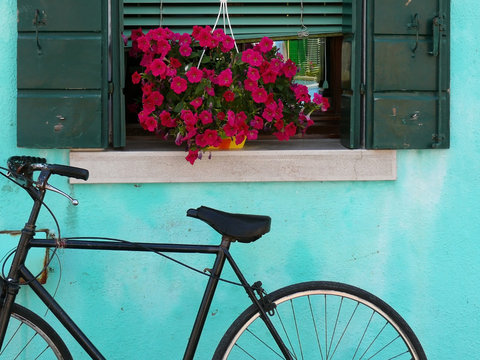 Bicicletta su parete azzurra e fiori sul balcone
