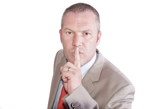 Middle aged businessman in suit makes gesture to be quiet