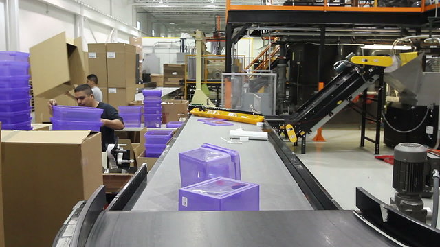 An assembly line conveyor belt delivers plastic bins to workers who package them.
