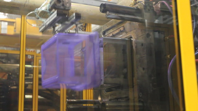In a factory, a plastic bin is manufactured and a robotic arm grabs it.

