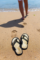 Beach slippers on sand, and female feet at a sea edge
