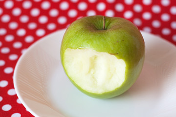 Green apple on a white plate on a red background