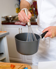 professional chef hands with kitchen utensils whisk and pan
