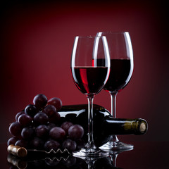 Wine in glasses with grape and bottle on red