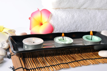 three candles in plate with white towel and plumeria on bamboo m