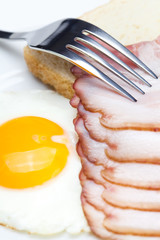 bacon with  fried  eggs on a plate, fork and bread isolated on w