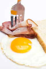 bacon with  fried  eggs on a plate, fork and bread isolated on w