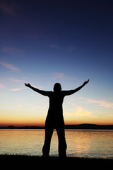 Young woman silhouette raised hands standing at coast