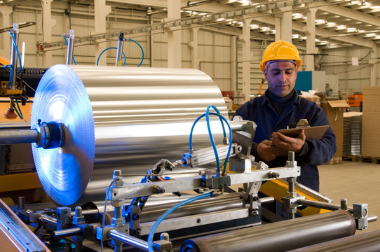 Factory worker processing roll of steel sheet.
