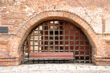 Часть старинной стены с аркой, решеткой и скамейкой.