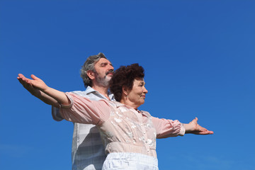old man and woman standing, smiling and looking at side