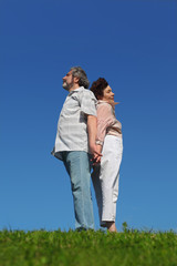 old woman and man standing on summer lawn back to back